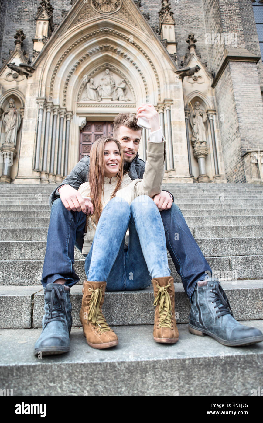 Volle Länge des jungen Paares nehmen Selfie auf Schritte im freien sitzend Stockfoto