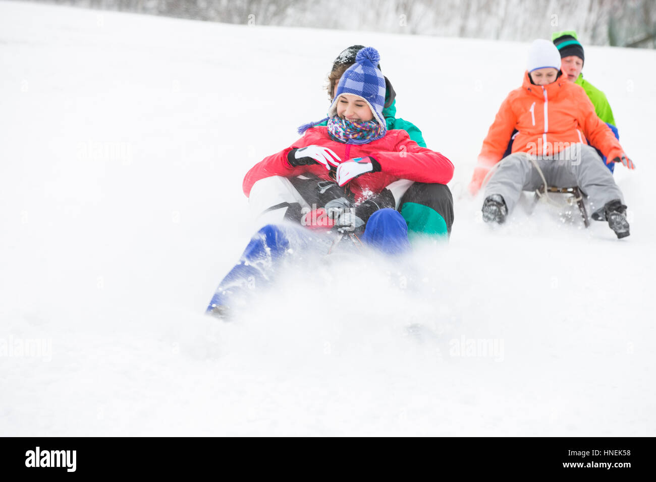 Junge Paare genießen Schlitten fahren auf Schnee bedeckten Hang Stockfoto
