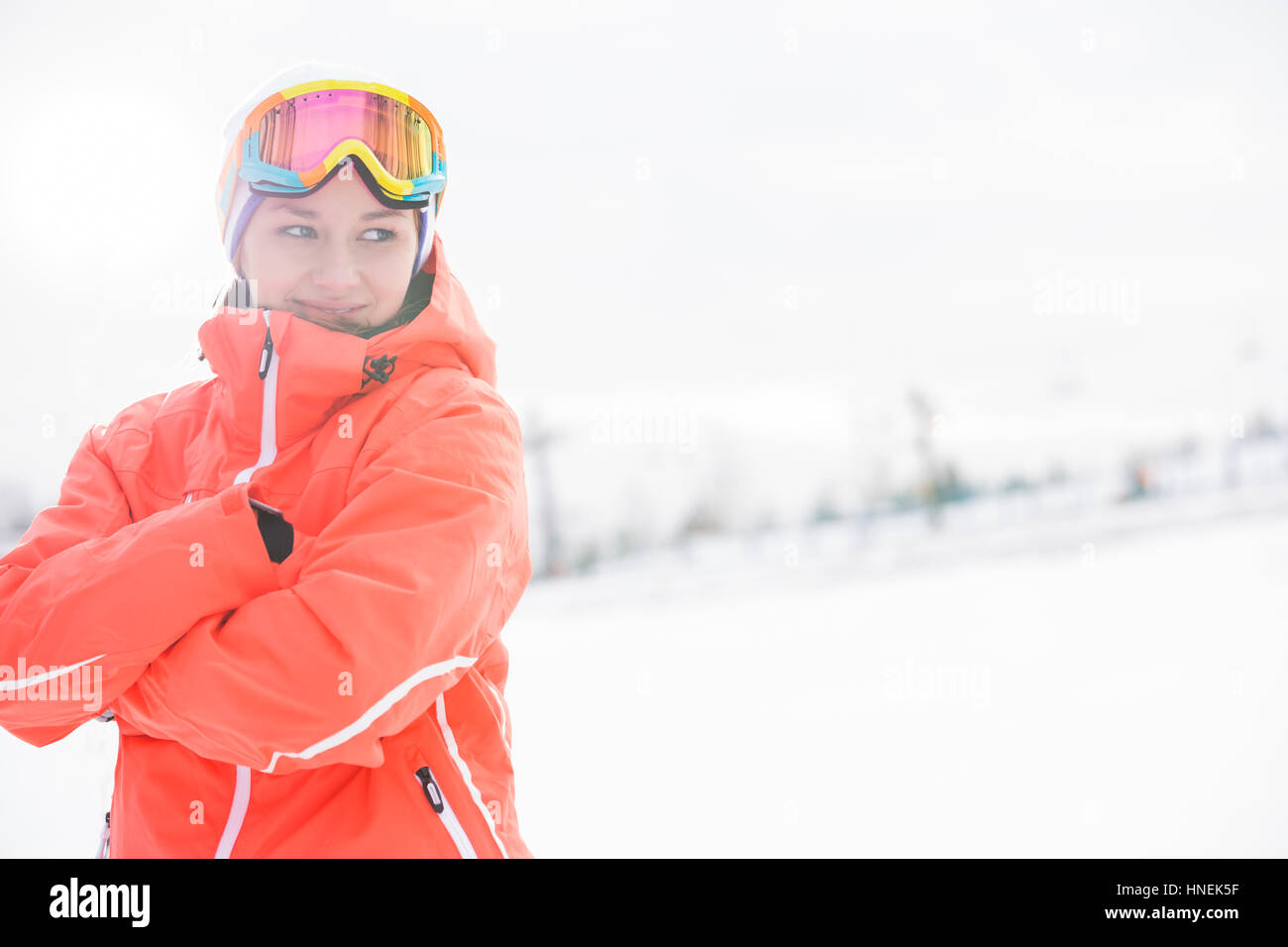 Glückliche junge Frau in warme Kleidung stehend Arme gekreuzt auf schneebedecktes Feld Stockfoto