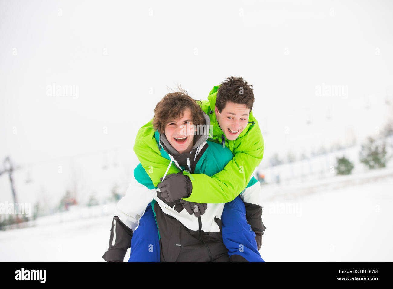 Junge männliche Freunde genießen Huckepack Reiten im Schnee Stockfoto