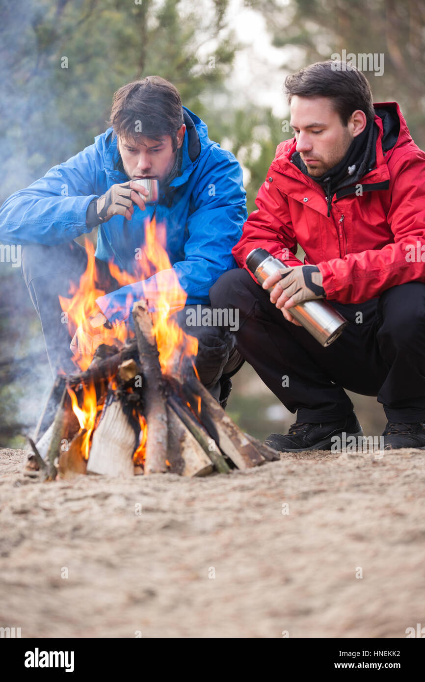 Männliche Rucksacktouristen Kaffeetrinken am Lagerfeuer im Wald Stockfoto