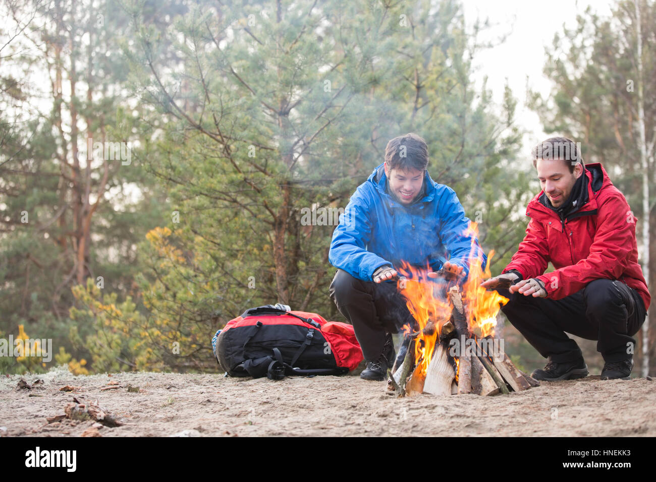 Männliche Rucksacktouristen, die Erwärmung der Hände am Lagerfeuer im Wald Stockfoto