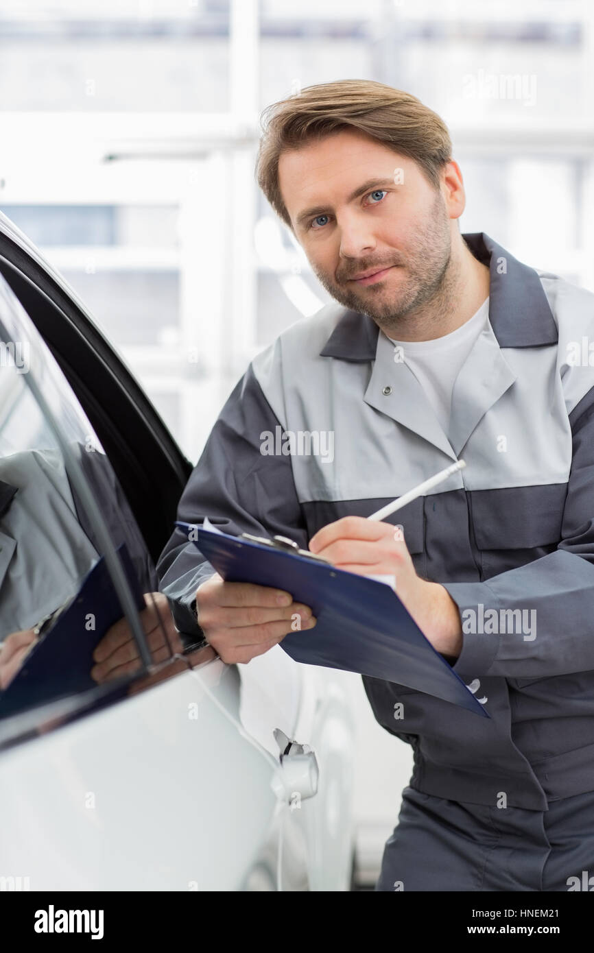 Porträt von zuversichtlich Mechaniker Holding Zwischenablage beim stützte sich auf Autofenster in Werkstatt Stockfoto