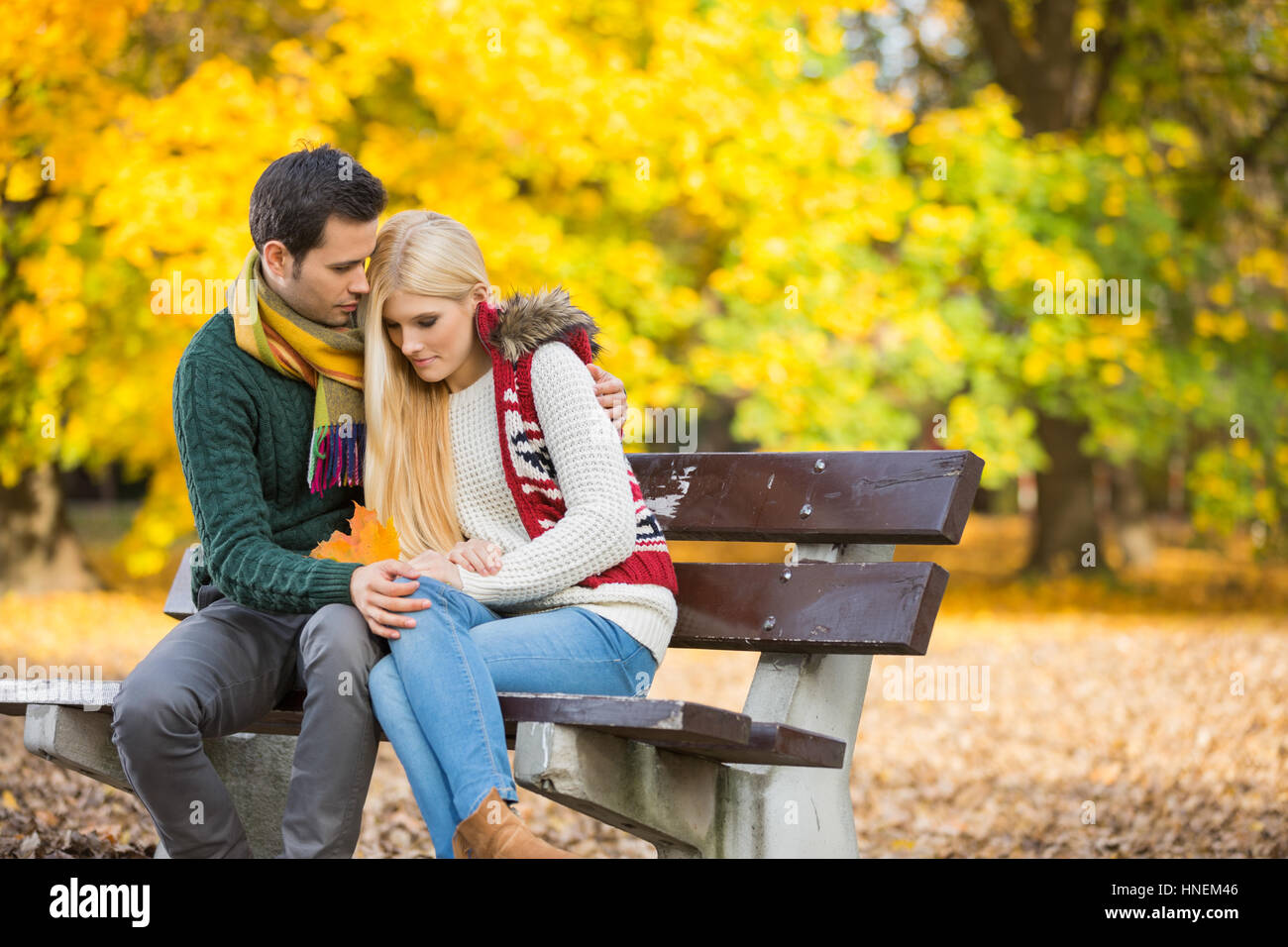 Leidenschaftlicher junger Mann umarmt schüchterne Frau auf Parkbank im Herbst Stockfoto