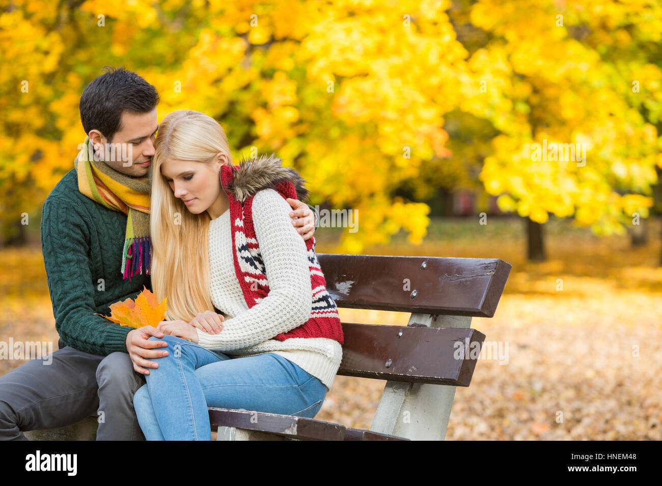 Liebevoller junger Mann umarmt schüchterne Frau auf Parkbank im Herbst Stockfoto