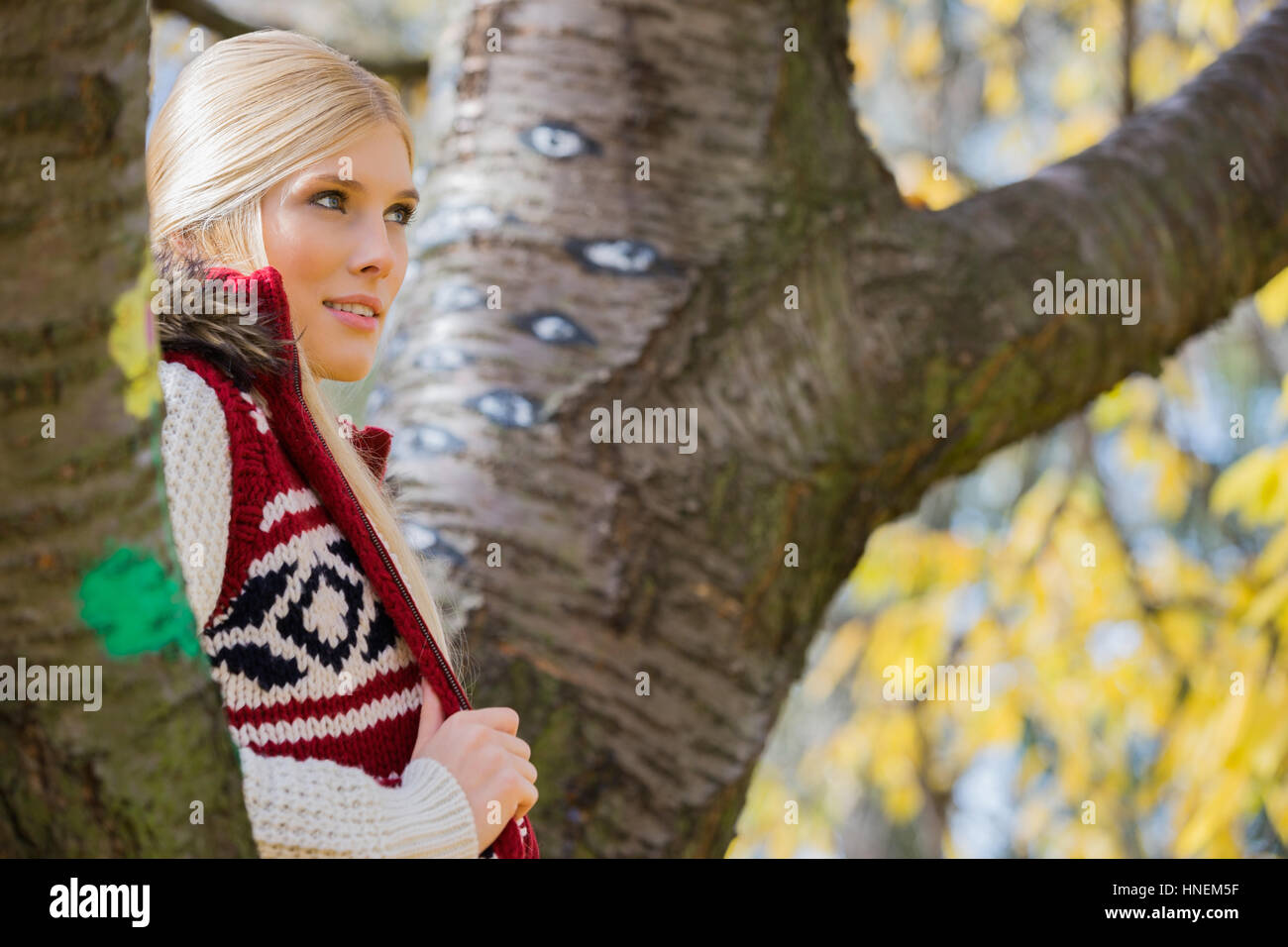 Nachdenkliche junge Frau in warme Kleidung stehen in der Nähe von Bäumen im park Stockfoto