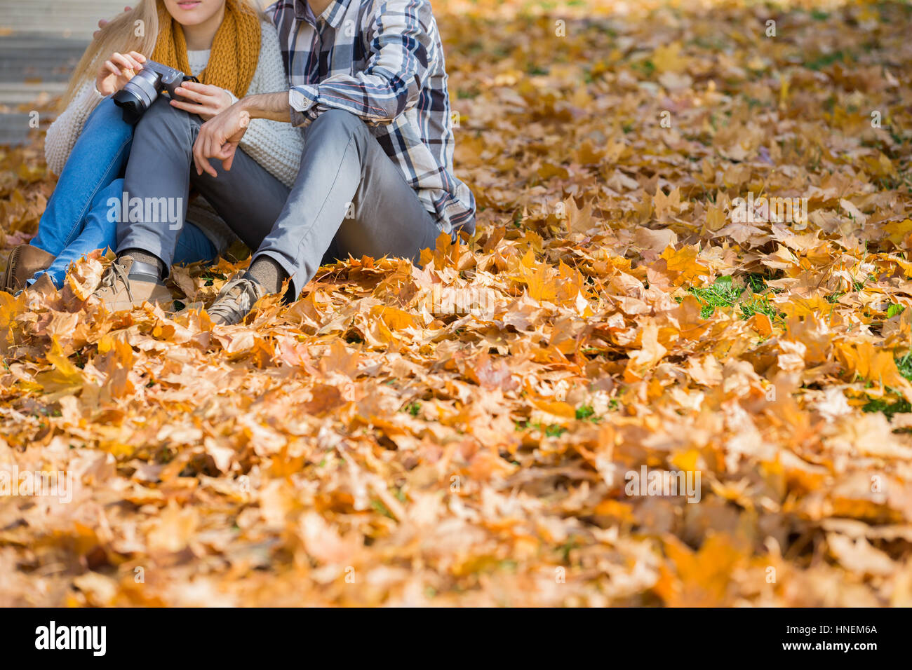 Niedrige Abschnitt des Paares mit Kamera sitzt auf Herbst Blätter im park Stockfoto Niedrige Abschnitt des Paares mit Kamera sitzt auf Herbst Blätter im park Stockfoto