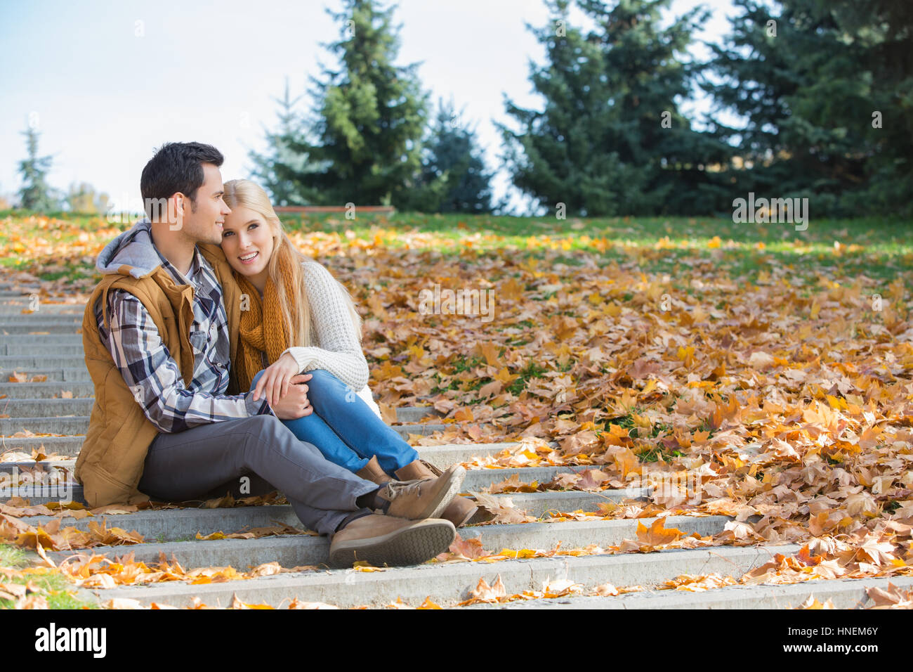 Liebende Paar umarmt sitzend auf Schritte im Park im Herbst Stockfoto