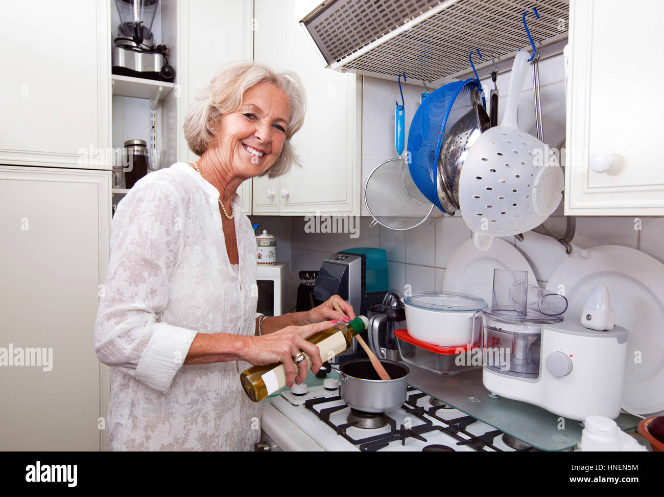 Porträt von senior Frau Topf am Küchentisch Olivenöl hinzufügen Stockfoto