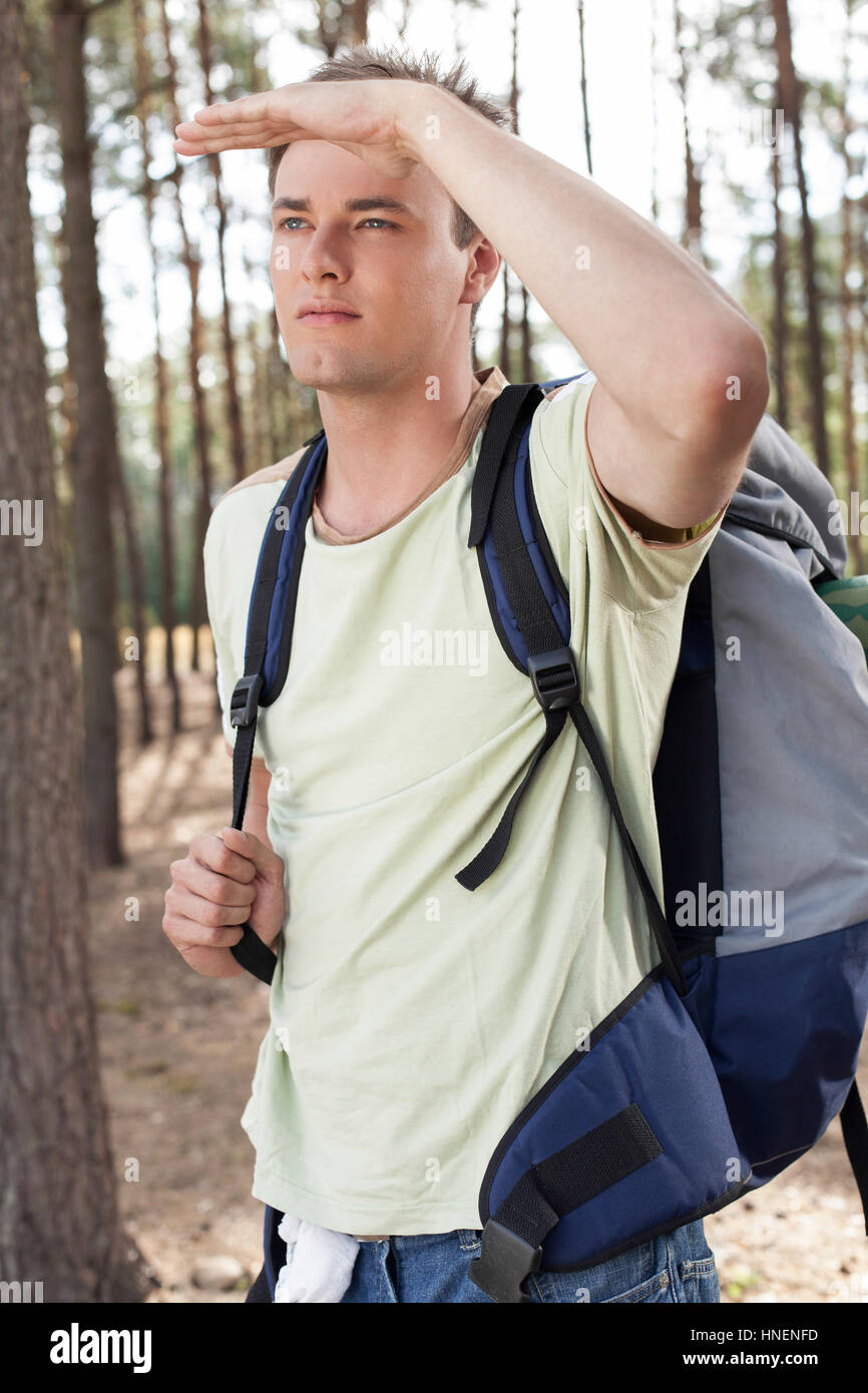 Junger Mann mit Rucksack Abschirmung Augen im Wald Stockfoto