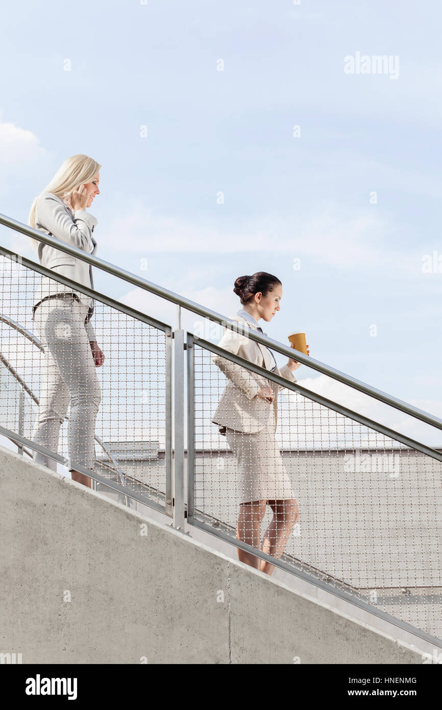 Profil-Schuss von Geschäftsfrauen, die beweglichen Treppen gemeinsam gegen Himmel Stockfoto