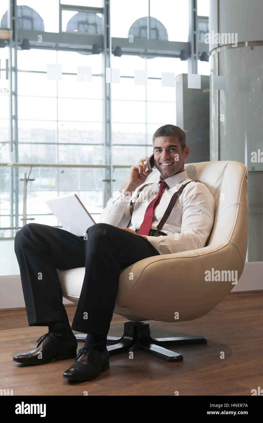 Geschäftsmann in Sessel arbeiten am Laptop auf dem Handy Stockfoto