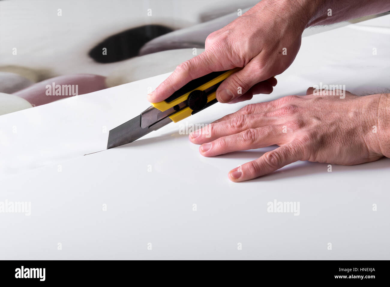 Designer männliche Hände Nahaufnahme Kürzungen des weißen breiten Blatt Papier mit BRAdmin professional Messer cutter Stockfoto