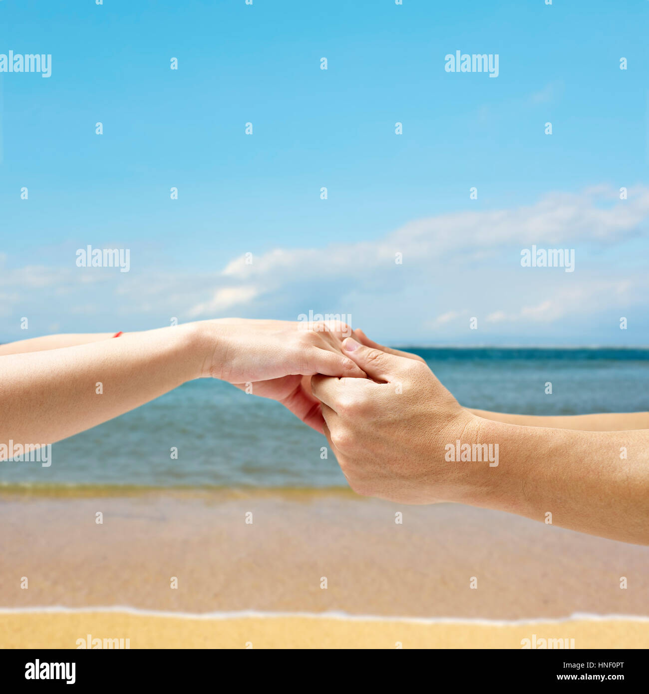 Hände eines jungen Paares, Himmel, Meer und Strand im Hintergrund zusammengehalten. Stockfoto