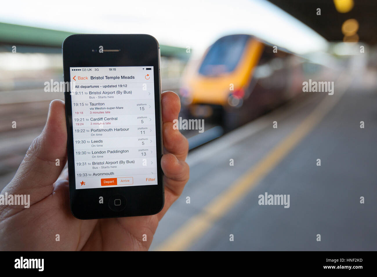 BRISTOL, UK - 8. April 2014: Eine männliche Hand, die ein iPhone am Bahnhof Bristol mit einem Zug im Hintergrund. Das Smartphone zeigt live tr Stockfoto