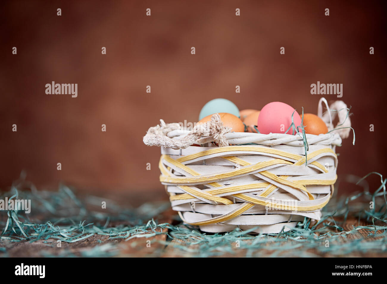 Korb und Rasen Onwooden Ostertisch vor braunen Wand Stockfoto