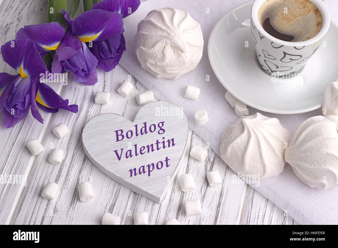 Stillleben mit Tasse Kaffee Marshmallow Zephyr Iris Blumen Herzschild mit Schriftzug Happy Valentines Day in Ungarisch auf weißem Hintergrund aus Holz. W Stockfoto