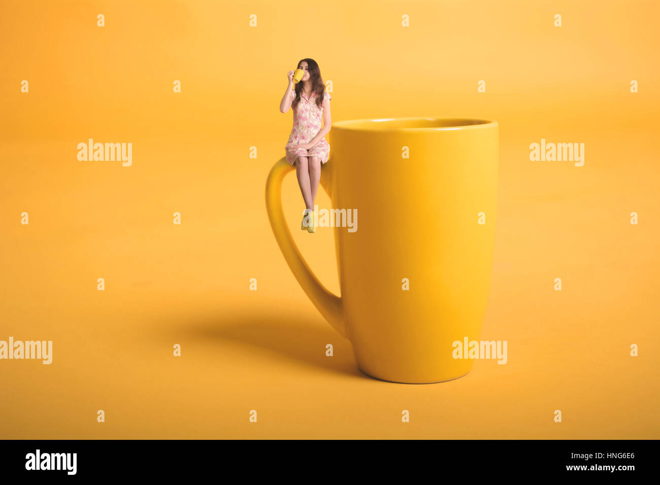 Kreative Surrealismus Design mit Miniatur-Menschen. Mädchen mit einer Tasse. Das Mädchen im rosa Kleid sitzt auf der Tasse. Gelbe Tasse Tee oder Kaffee. Junge Frau Stockfoto
