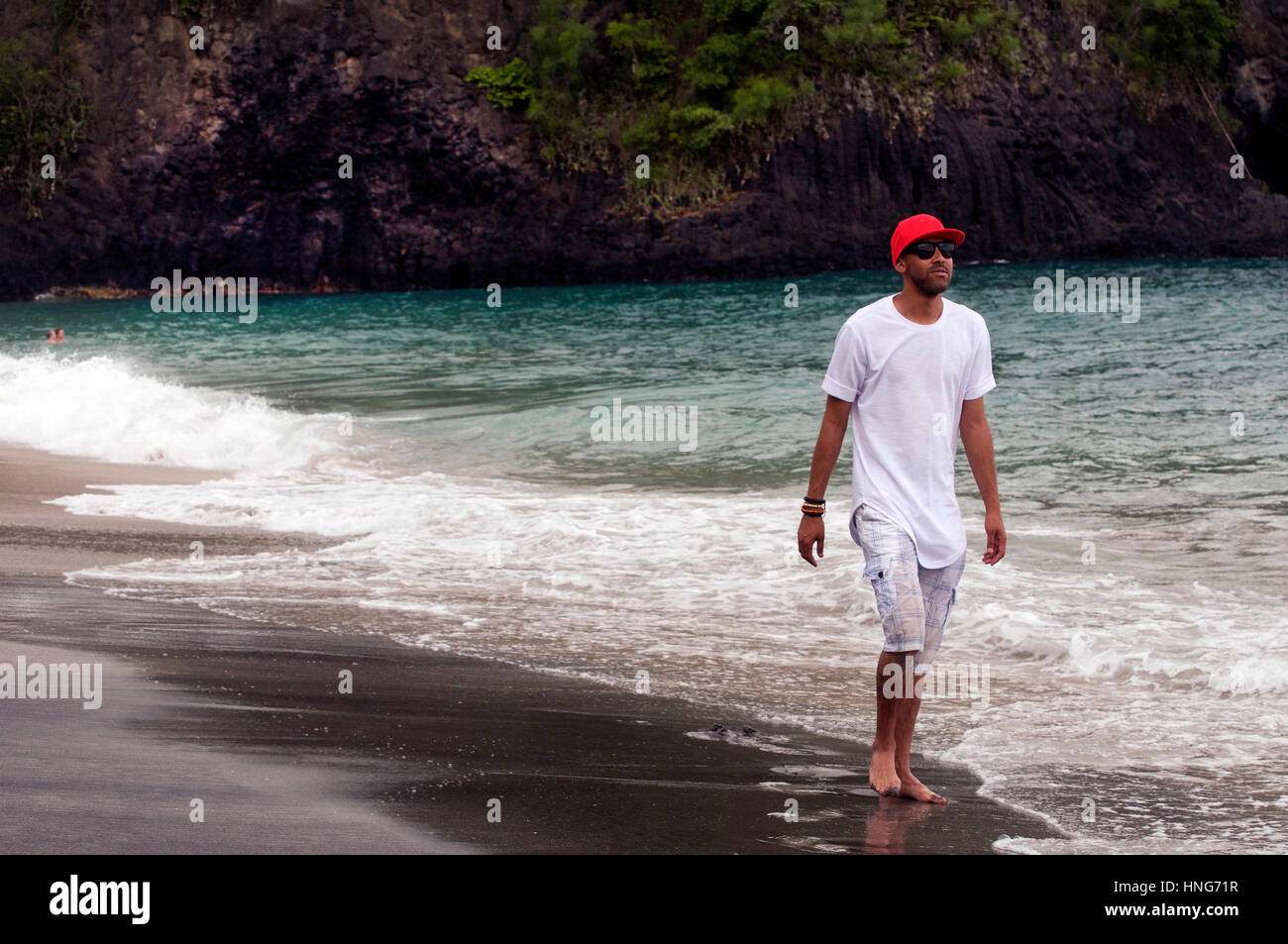 Cooler Typ Spaziergänge entlang Sandy Beach in Bali Indonesien tragen rote Baseballkappe, weißes T-Shirt und kurze Hosen Stockfoto