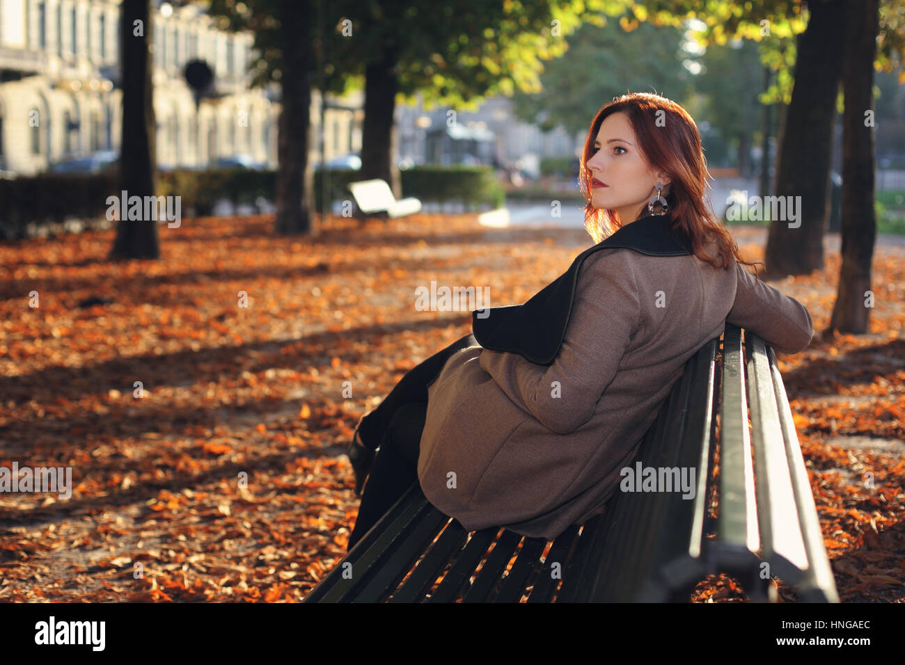 Schöne rote kurzhaarige Frau auf einer Bank im park Stockfoto