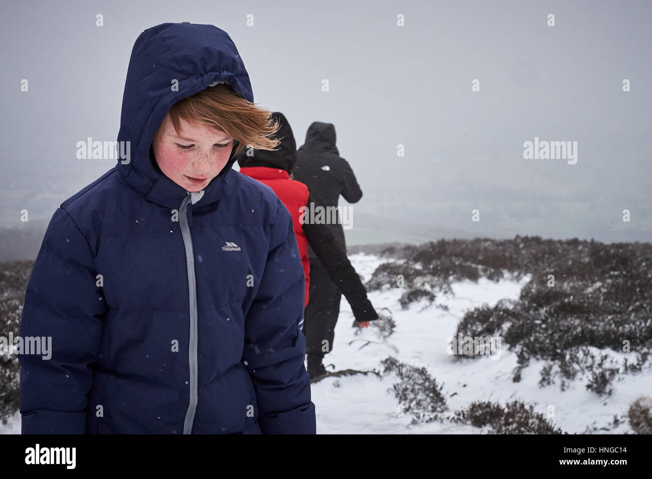 Ein Mädchen wickelte sich warm an einem kalten, winterlichen Tag, der im Schnee auf einem Hügel ging Stockfoto