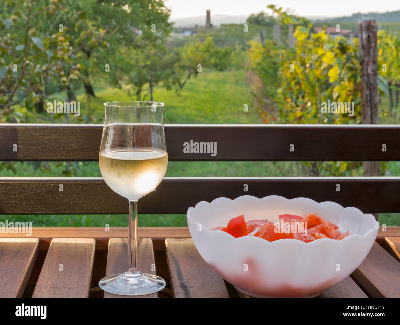 Glas Weißwein und frischen Tomaten Salat auf Holztisch mit unscharfen malerischen mediterranen Ausblick im Hintergrund. Brda Region, Western Sl Stockfoto