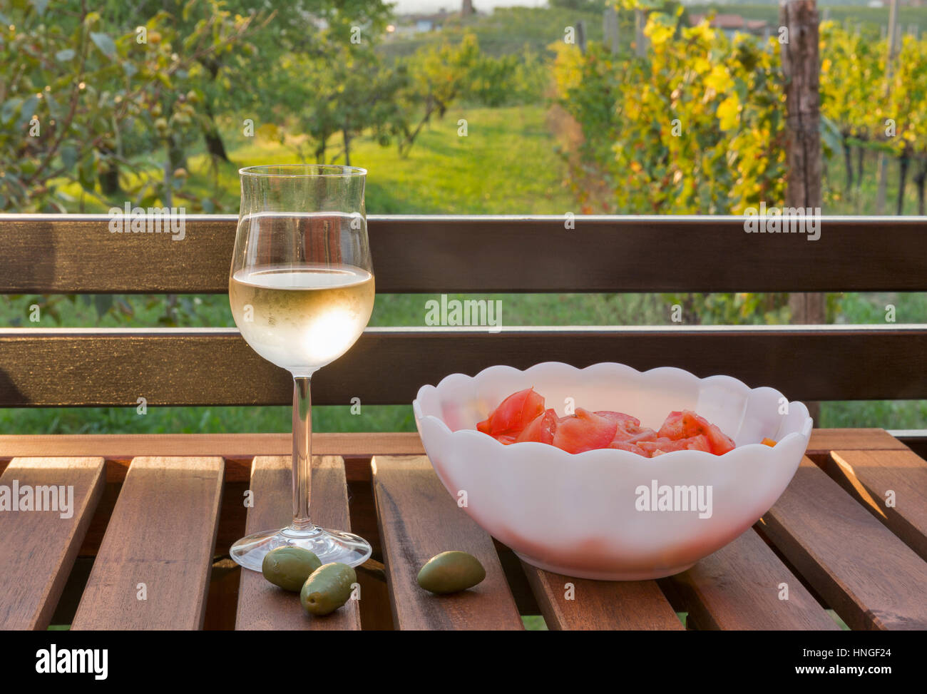 Glas Weißwein, grünen Oliven und frischen Tomaten Salat auf Holztisch mit unscharfen malerischen mediterranen Ausblick im Hintergrund. Brda regi Stockfoto