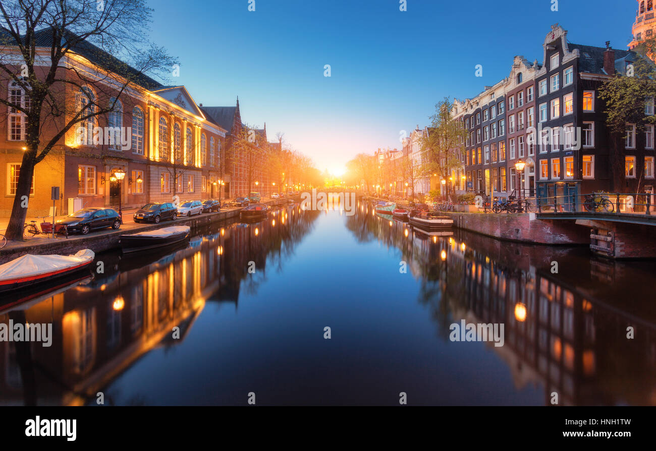 Bunte Stadtbild bei Sonnenuntergang in Amsterdam, Niederlande. Spiegelt sich die Lichter der Stadt im Wasser mit blauem Himmel in der Dämmerung. Nachtbeleuchtung von Gebäuden und Stockfoto