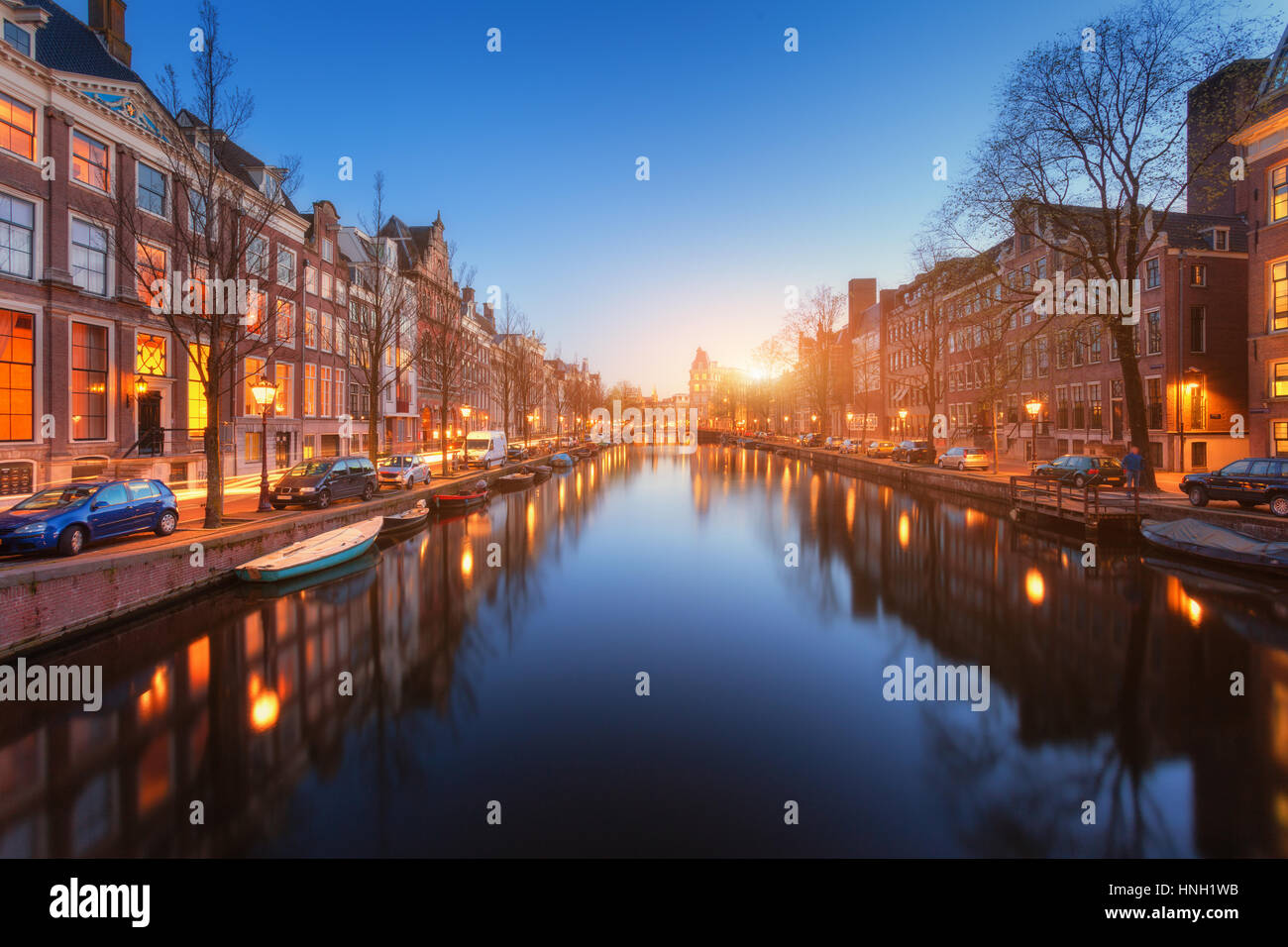 Bunte Stadtbild bei Sonnenuntergang in Amsterdam, Niederlande. Spiegelt sich die Lichter der Stadt im Wasser mit blauem Himmel in der Dämmerung. Nachtbeleuchtung von Gebäuden und Stockfoto