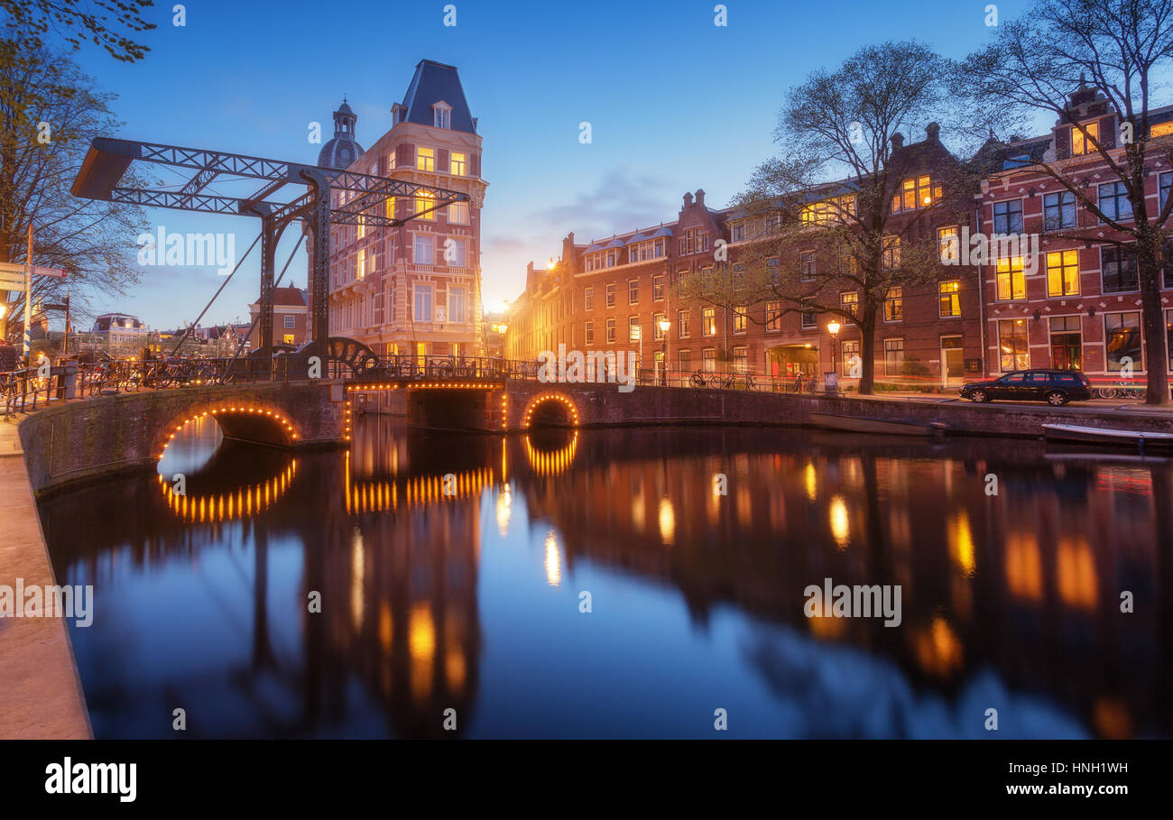 Bunte Stadtbild bei Sonnenuntergang in Amsterdam, Niederlande. Spiegelt sich die Lichter der Stadt im Wasser mit Sonnenlicht und blauem Himmel in der Dämmerung. Nachtbeleuchtung von b Stockfoto