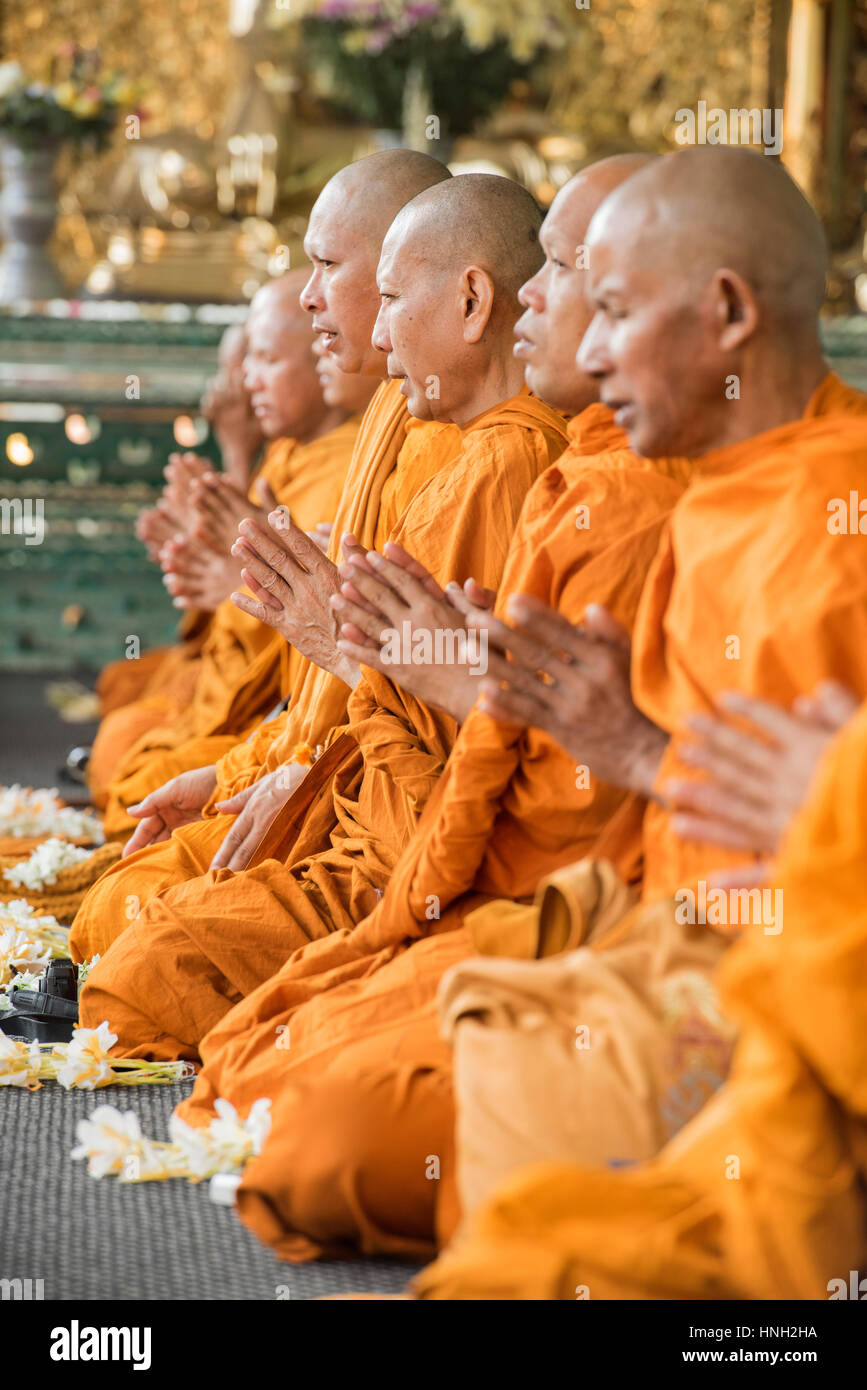Buddhistische Mönche in orangefarbenen Gewändern zeigen großen Konzentration in einem Tempel zu beten, während auf dem Boden im halben Lotussitz sitzen Stockfoto