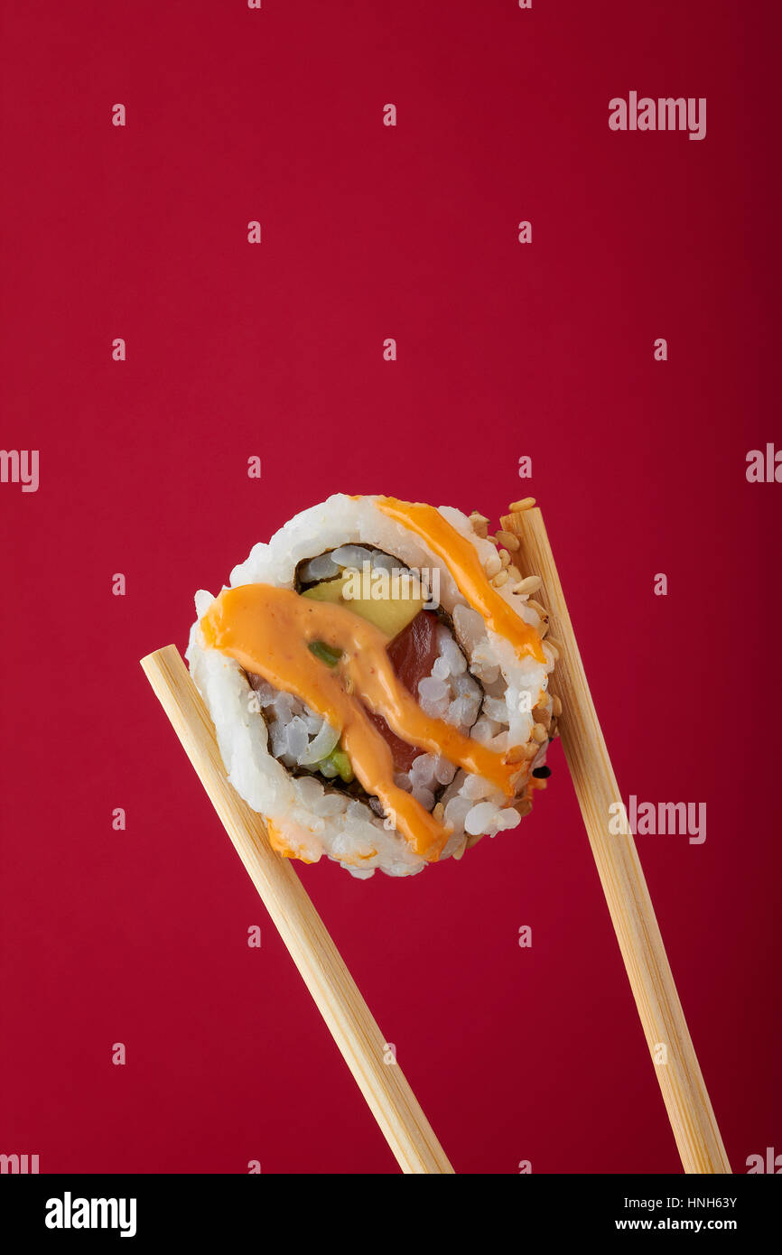 Einzigen Stück Sushi in hölzernen Stäbchen vor einem roten Hintergrund statt Stockfoto