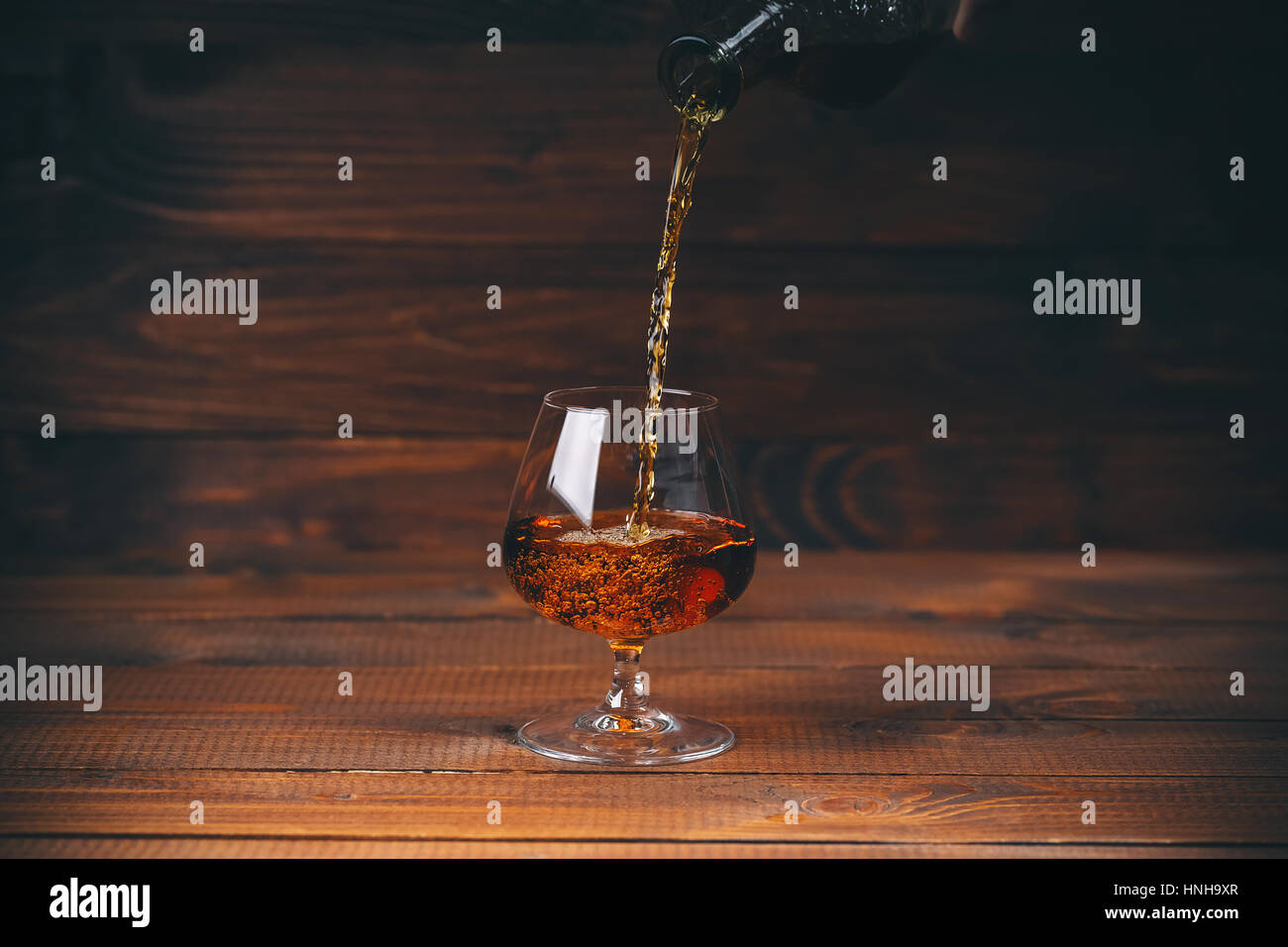 Weinbrand oder Cognac aus der Flasche in das Glas Holz Hintergrund gießen Stockfoto