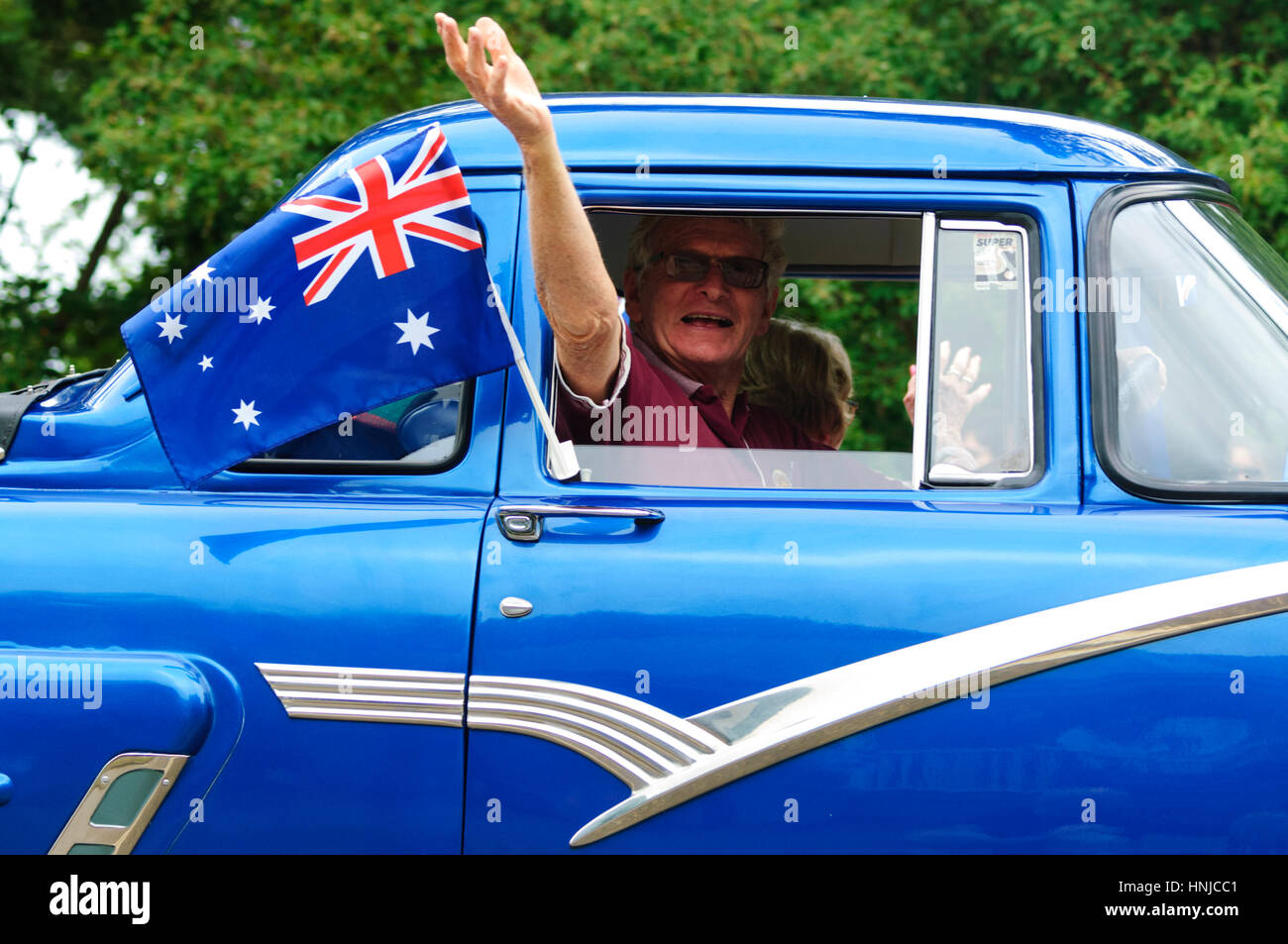 Mann aus einem blauen Oldtimer mit einer australischen Flagge winken beteiligt sich an der Australia Day 2017 Parade, Berrima, New-South.Wales, Australien Stockfoto