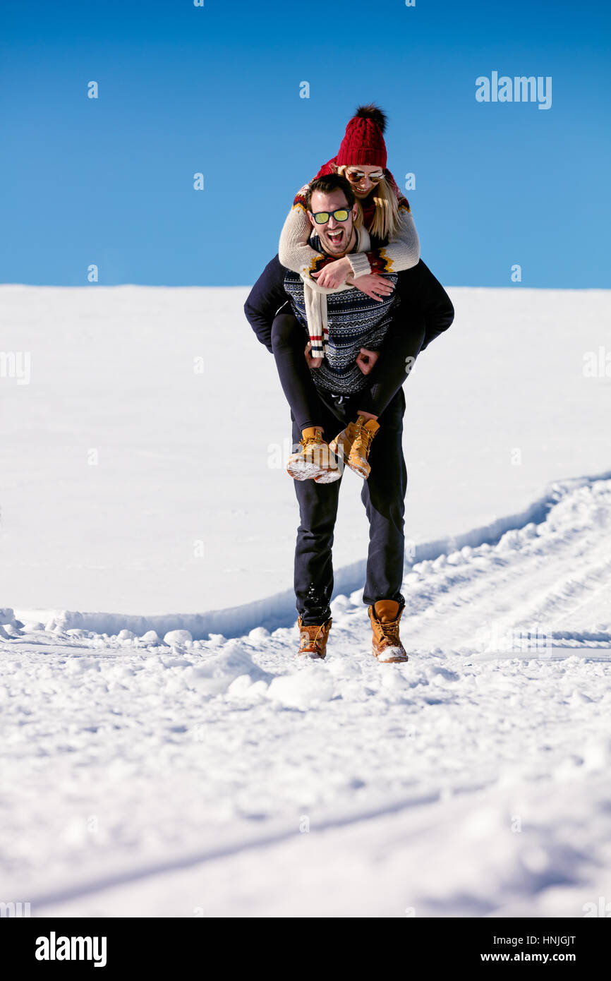 Paar im Schnee spielen. Mann und Frau Huckepack Fahrt im Winterurlaub. Stockfoto