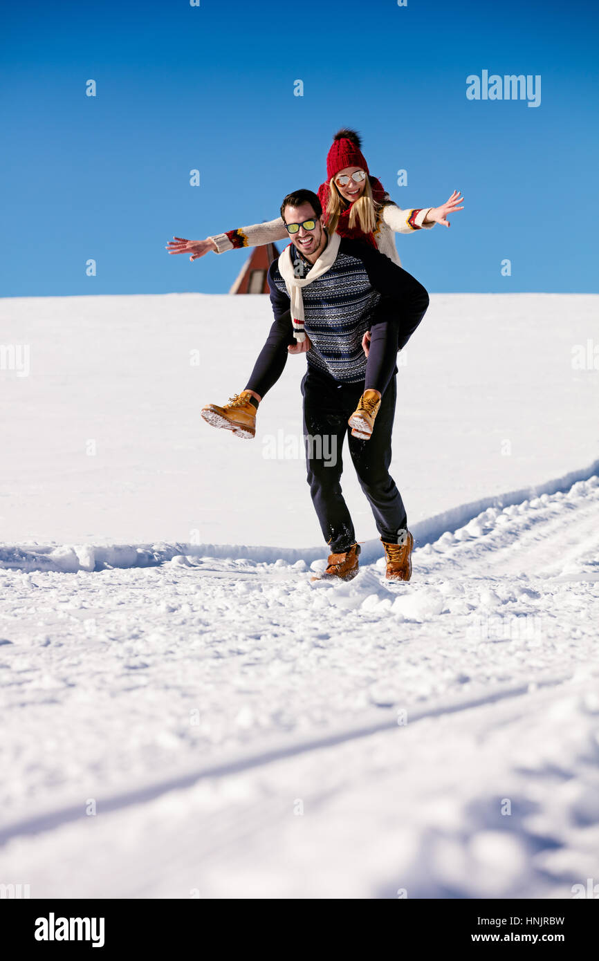 Paar im Schnee spielen. Mann und Frau Huckepack Fahrt im Winterurlaub. Stockfoto