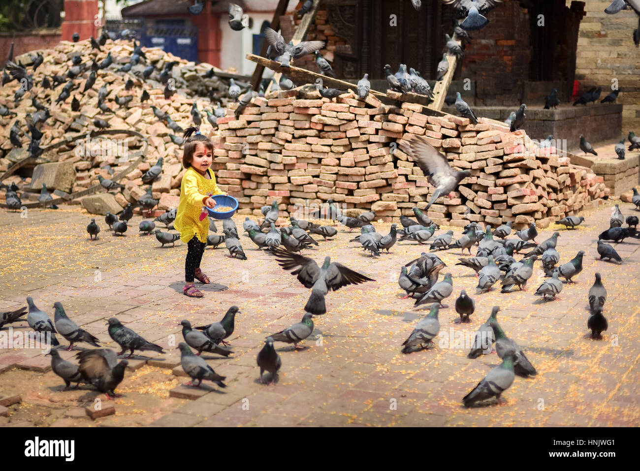 Ein kleines Mädchen füttert eine Herde Tauben in der Nähe der Ruinen eines antiken Tempels in Kathmandu, Nepal. Stockfoto