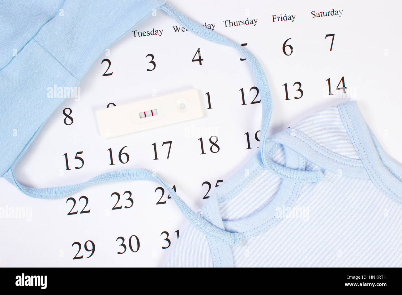 Schwangerschaftstest mit positivem Ergebnis und Kleidung für Neugeborene auf Kalender, Konzept der Familie erweitern und erwartet für baby Stockfoto