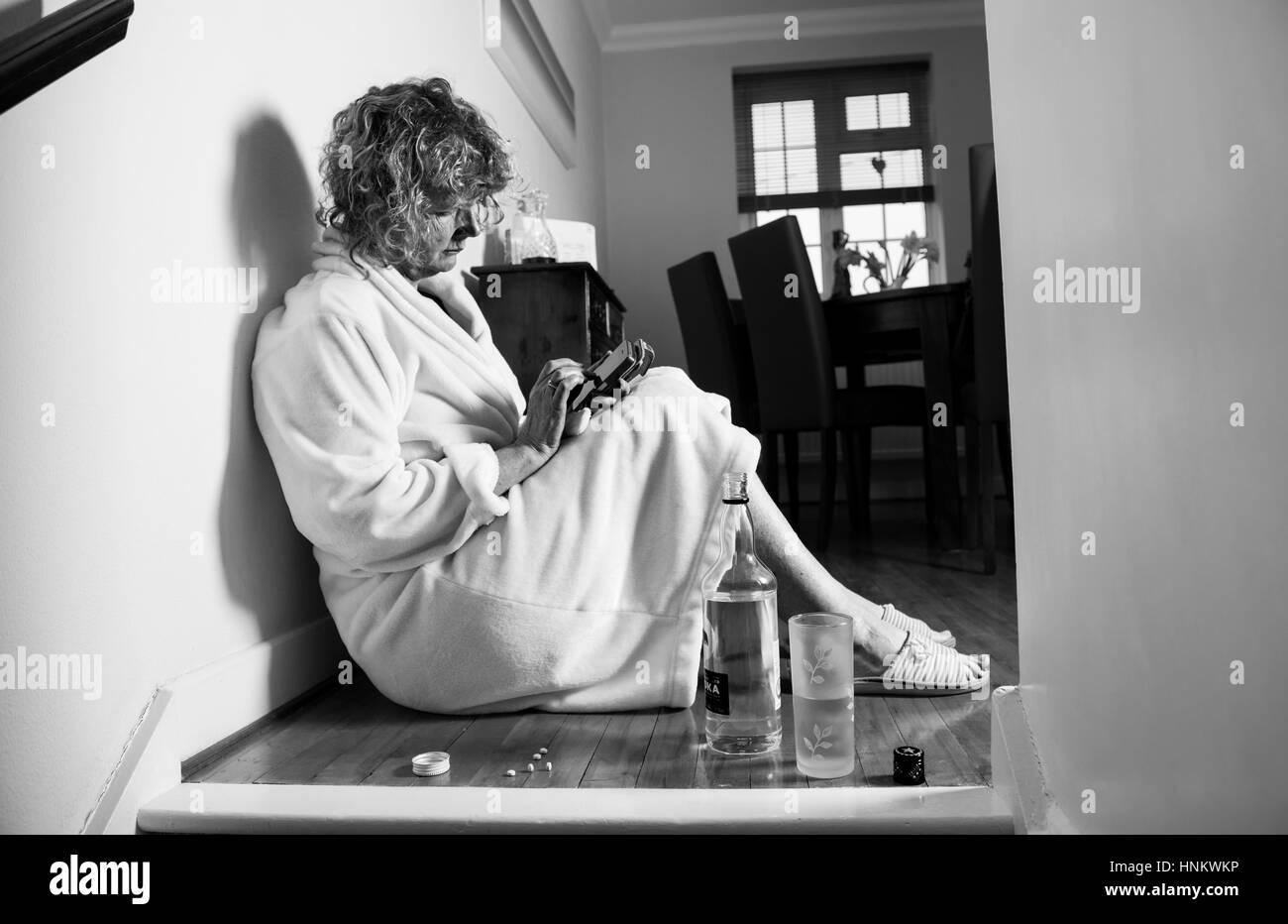 Depressive Frau im Morgenmantel zu Hause tagsüber behandeln stark trinken und Einnahme von Tabletten zu sich selbst telefonieren für Hilfe - trefffen Modell Stockfoto