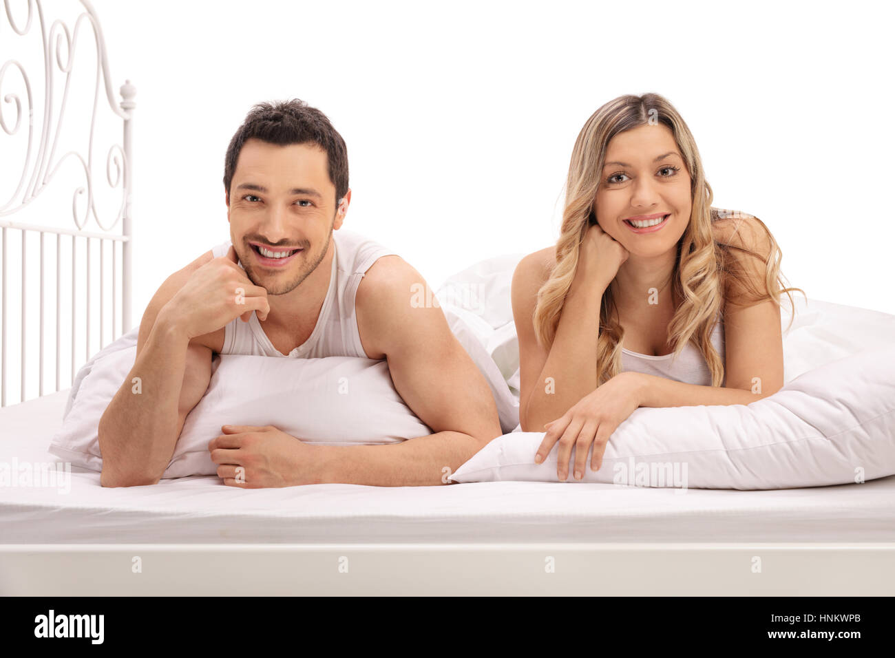 Glückliches junges Paar im Bett liegen und schaut in die Kamera, die isoliert auf weißem Hintergrund Stockfoto