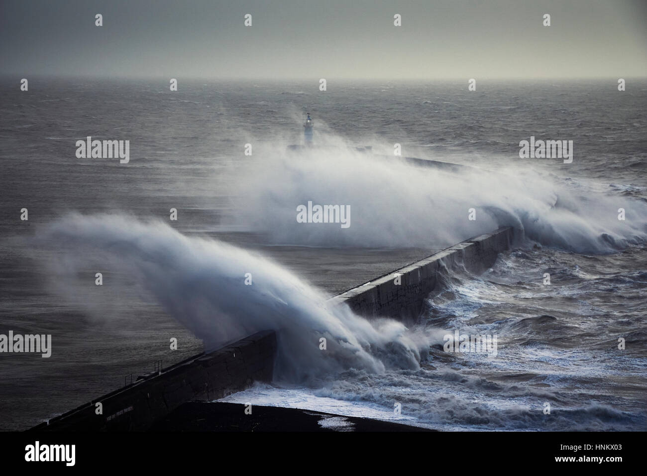 Riesige Wellen über einen Deich in der Nähe von einem Leuchtturm während eines Sturms Stockfoto