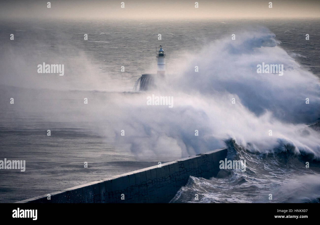 Riesige Wellen über einen Deich in der Nähe von einem Leuchtturm während eines Sturms Stockfoto