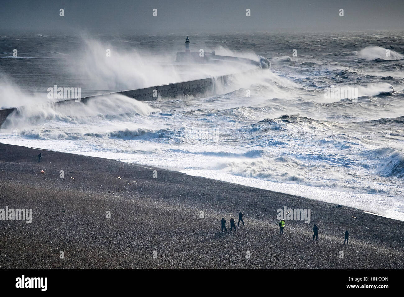 Menschen wachen vom Strand als riesige Wellen über einen Deich in der Nähe von einem Leuchtturm während eines Sturms Stockfoto