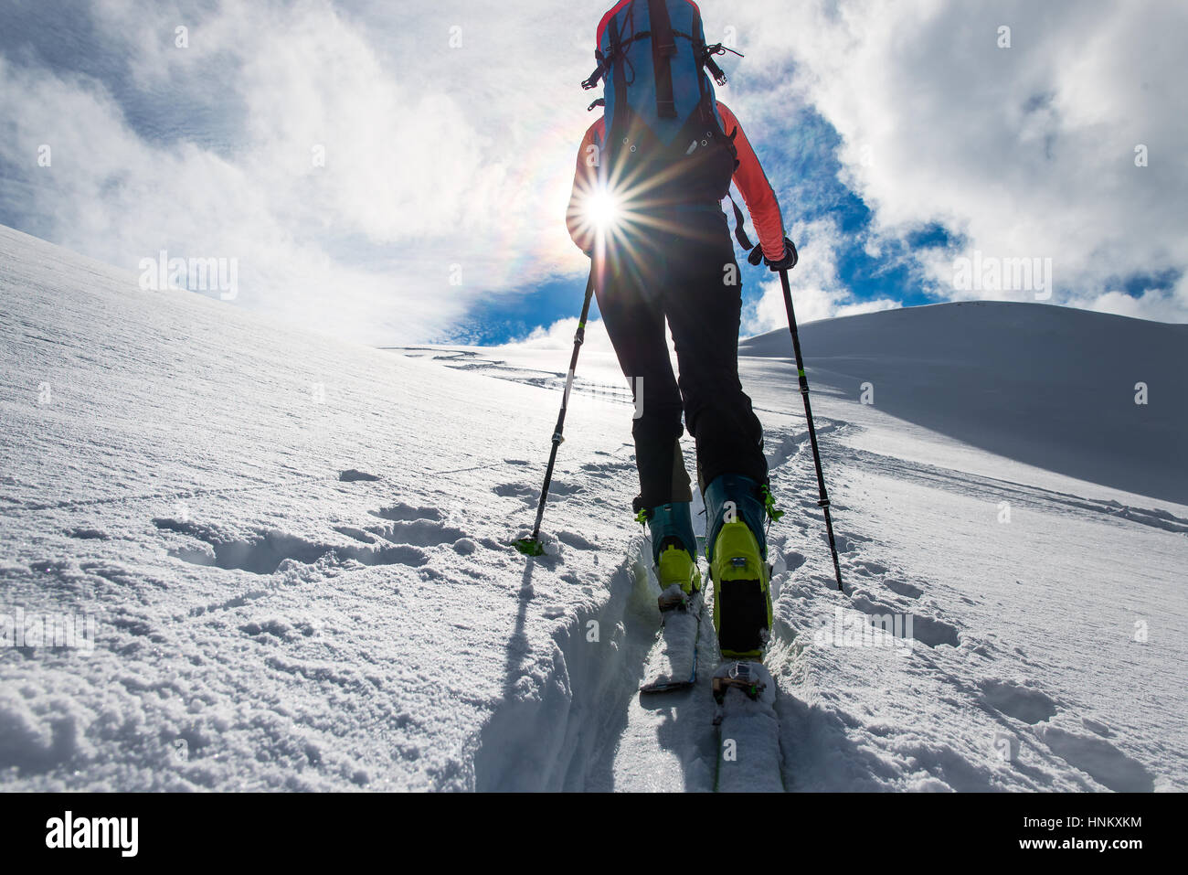 Mädchen-Bergsteiger steigen auf Skiern und Fellen in Richtung der Sonne Stockfoto