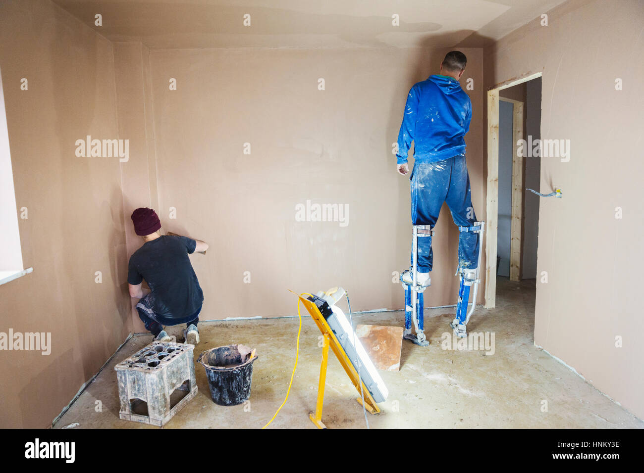 Ein Elektriker und Gipser arbeiten an den Wänden eines Hauses im Bau. Stockfoto