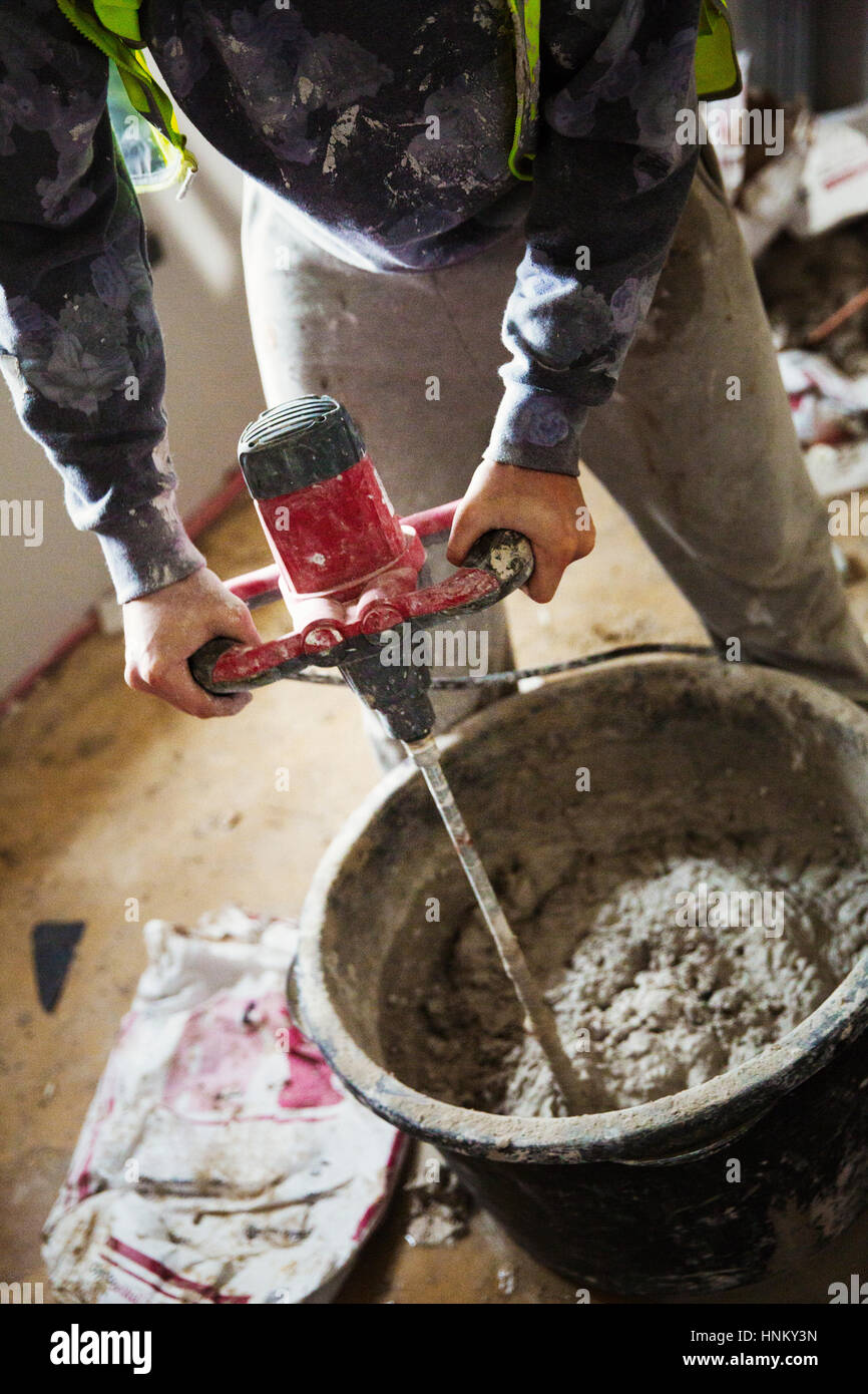 Ein Baumeister mischen Gips mit einem elektrischen Mixer in einem Eimer auf einer Baustelle. Stockfoto
