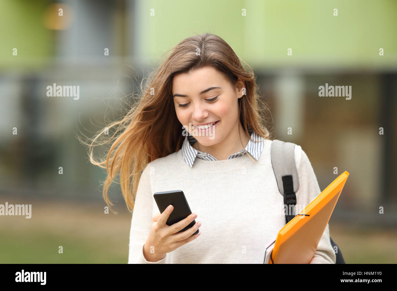 Einzelne Schüler Wandern und lesen Handy-Nachrichten mit einem Universitätsgebäude im Hintergrund Stockfoto