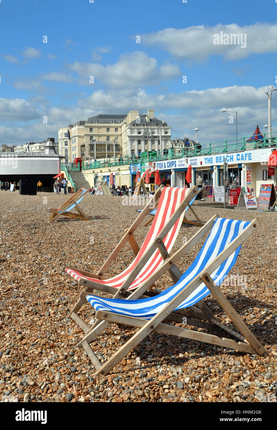 Brighton, Vereinigtes Königreich - 16. April 2012: rot & blau gestreifte Liegestühle erwarten die Touristen am Strand bei einem Frühlingstag in Brighton. Stockfoto