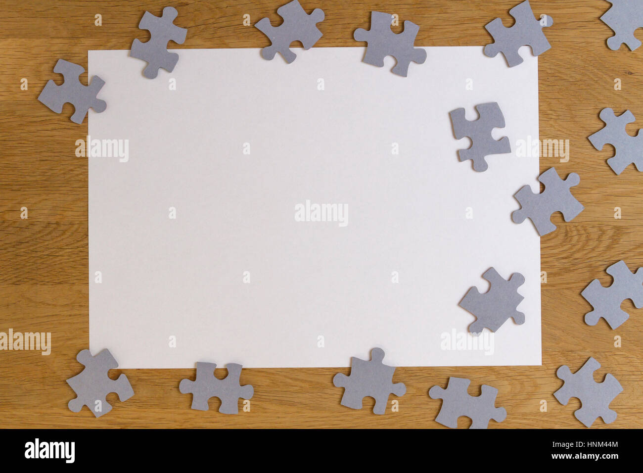Leeres weißes Blatt Papier, die Puzzleteile auf hölzernen Hintergrund umgeben. Ansicht von oben. Platz für Text kopieren Stockfoto