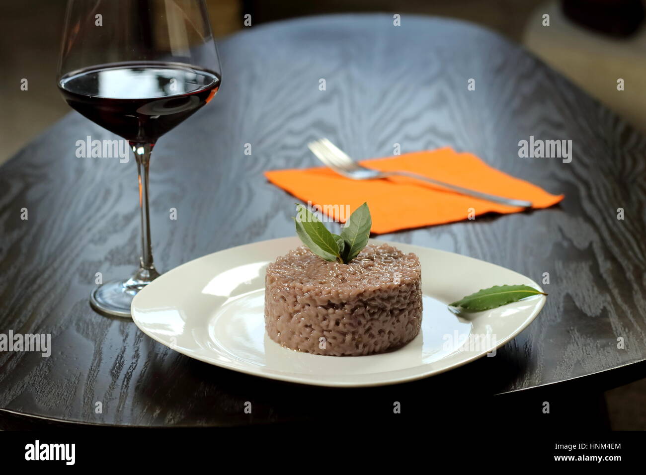 Vegetarische rot Wein Risotto (Chianti oder Barolo) in weiße Schale auf dunklen Holztisch - italienische Küche-Rezept - Lorbeerblatt auf Oberseite und Glas Rotwein Stockfoto